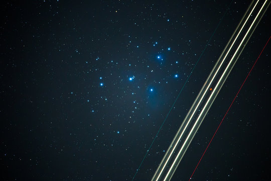 Ein Flugzeug fliegt in der Nacht, im Hintergrund sind die Sterne der Plejaden zu sehen