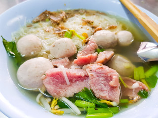 Asian style beef noodle soup,white rice noodle in clear soup with homemade meat balls and medium rare beef slides and vegetable in the bowl with soup spoon and chopstick