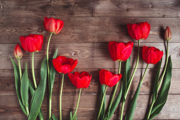 Row of red tulips on wooden background with space for message. Women's or Mother's Day background. Top view