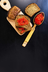 spoon of red caviar and a sandwich on a black background