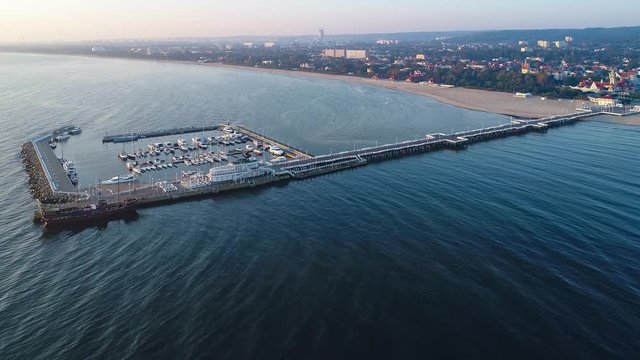 Sopot resort in Poland. Wooden pier (Molo) with promenade, marina, yachts, pirate tourist ship, beach, old lighthouse, SPA, hotels and vacation infrastructure. Aerial 4K video at sunrise