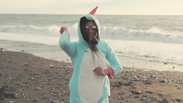 Happy beautiful girl is dancing and enjoying life on the beach in the evening. She is wearing unicorn kigurumi.