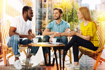 Friendly people. Young friendly emotional people spending time together in a pleasant cafe with cups of coffee on a little table and looking glad while communicating