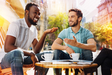 Interesting story. Cheerful positive smiling student being in a good mood while sitting with his friends and telling them and amazing story