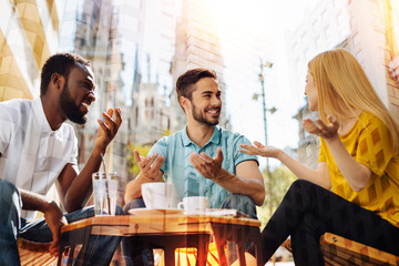 Funny story. Positive friendly young people having a good time in a lovely cafe and laughing while looking at their fellow student and listening to her funny story