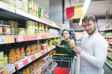 Young beautiful pair posing in a supermarket with products in their hands. A young man and a girl buy canned vegetables in a supermarket
