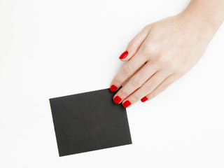 Flat lay, top view. Beauty and fashion concept. Beautiful female hands with red manicure. Minimal style. Minimalist photography. Pale composition with girl's hand holding card on white background