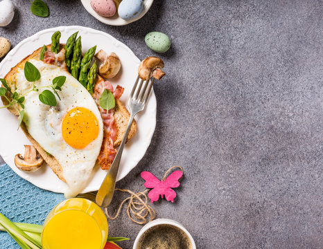 Easter breakfast flat lay with bread toast with fried egg and green asparagus, orange tulips, , colored quail eggs and spring holidays decorations. Top view. Copy space.