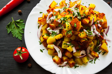 fried potatoes with bacon and onion in a plate on a dark wooden background