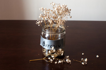 A bitcoin in a glass jar filled with gold coins and dried flower