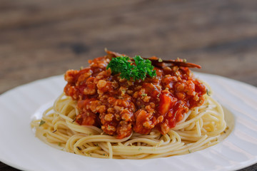 Spaghetti bolognese sauce with beef or pork,cheese,tomatoes and spices on white plate on wood table, side view with close up. Homemade delicious Italian traditional food for lunch or dinner.