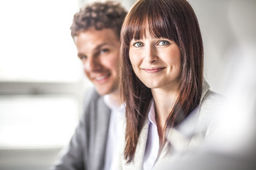 Portrait of beautiful young businesswoman with male colleague in background at office