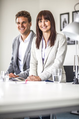 Portrait of young businesswoman with male colleague at table in office