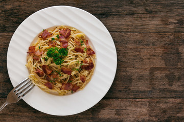 Spaghetti carbonara with bacon, cheese and chopped parsley on wood table in top view flat lay with copy space. Italian traditional homemade food for lunch or dinner so creamy and delicious.