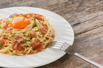 Spaghetti carbonara with bacon, cheese, yolk and sprinkle chopped parsley on wood table in side view with copy space. Italian traditional homemade food for lunch or dinner so creamy and delicious.