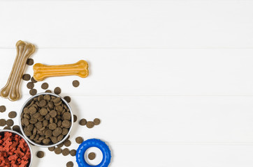 Dry dog pet food in bowl and accessories on white wooden background top view. Pet feeding and care concept backgrounds with copy space. Photograph taken from above.