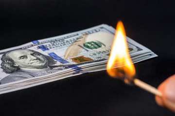 hand with match lights and hundreds dollars money On dark background. Concept devaluation,...