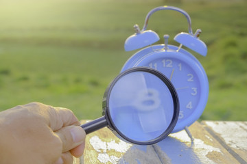 Alarm clock and magnifying glass standing on  wooen table against green background