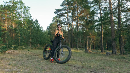 Fat bike also called fatbike or fat-tire bike in summer riding in the forest. Beautiful girl and her bicycle in the forest. She rolls her bike and poses to the operator.