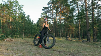 Fototapeta premium Fat bike also called fatbike or fat-tire bike in summer riding in the forest. Beautiful girl and her bicycle in the forest. She rolls her bike and poses to the operator.