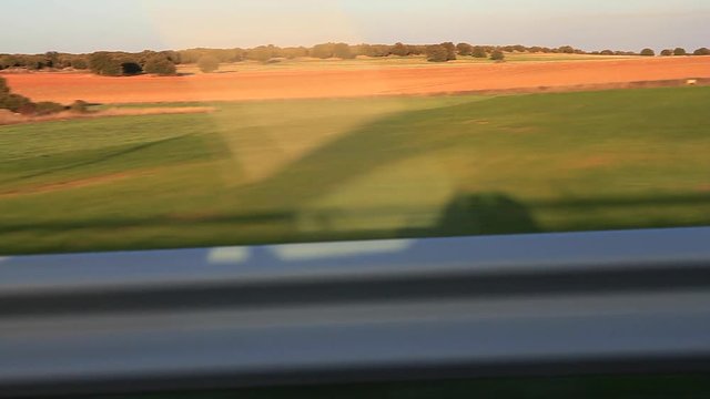 Traveling lateral de seguimiento  de la silueta en sombra del coche en paisaje de campos y encinas al atardecer
