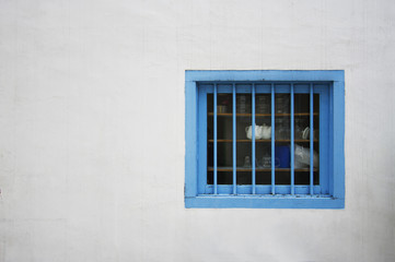 A square blue window hanging on a white side wall of a shop house.