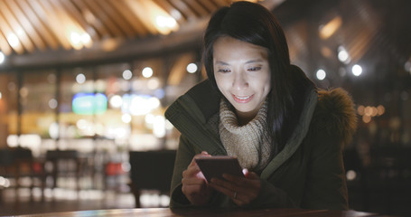 Woman using smart phone outside restaurant at night