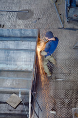 Worker uses angular grinding machine and carve out sparks. View from above
