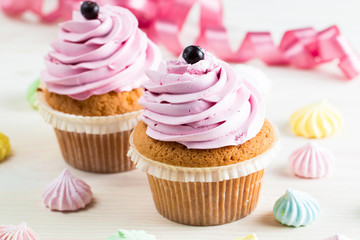 Closeup of cupcakes with vanilla, berries, pink and white cream, chocolate and sprinkles on wooden background. Selective focus. Sweet dessert tasty food concept muffin.