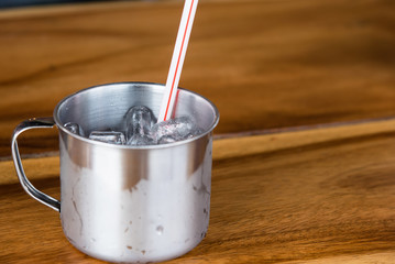 Ice in stainless cup of water on wooden table background.