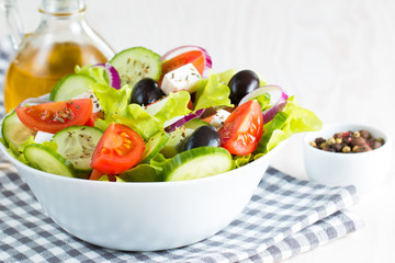Fresh Greek salad made of cherry tomato, ruccola, arugula, feta, olives, cucumbers, onion and spices. Caesar salad in a white bowl on wooden background. Healthy organic diet food concept.