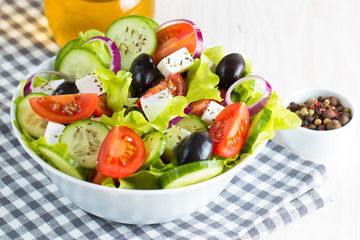 Fresh Greek salad made of cherry tomato, ruccola, arugula, feta, olives, cucumbers, onion and spices. Caesar salad in a white bowl on wooden background. Healthy organic diet food concept.