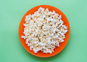 Fototapeta na wymiar Popcorn in an orange bowl on a green background. Top view