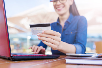 Shopping concept. Beautiful smiling young woman sits in front of a laptop and holds a bank card and...