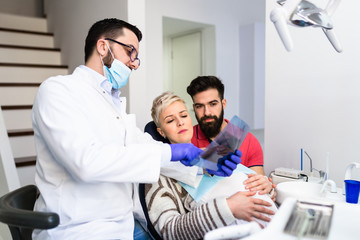 Obraz premium Attractive bearded man with his pregnant wife having medical treatment in dental office
