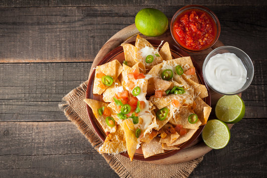 Corn Mexican nachos with beef, jalapeno, cheese, pepper, olives and chili con carne on a wooden background. Lime, Ketchup, sour cream and mayonnaise souce seasoning.