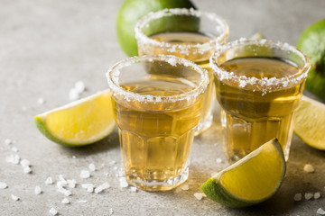 Macro focus photo of shots of golden Mexican tequila with lime and salt on wooden background....