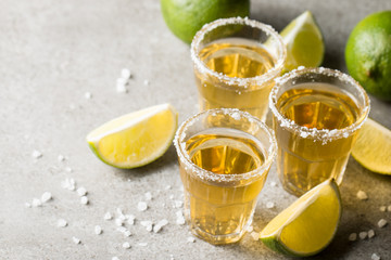 Macro focus photo of shots of golden Mexican tequila with lime and salt on wooden background. Alcoholic drink concept.
