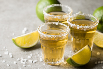 Macro focus photo of shots of golden Mexican tequila with lime and salt on wooden background....