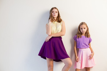 two girls posing with bright fashionable dresses on a white background