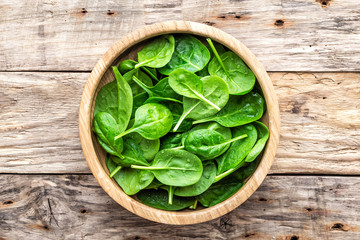 Fresh baby spinach leaves in bowl on wooden background