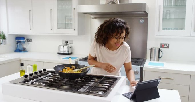 4K Cheerful woman cooking a meal at home, following a recipe on computer tablet