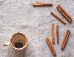Cinnamon, cloves, and a Cup of coffee on a rough burlap background.
