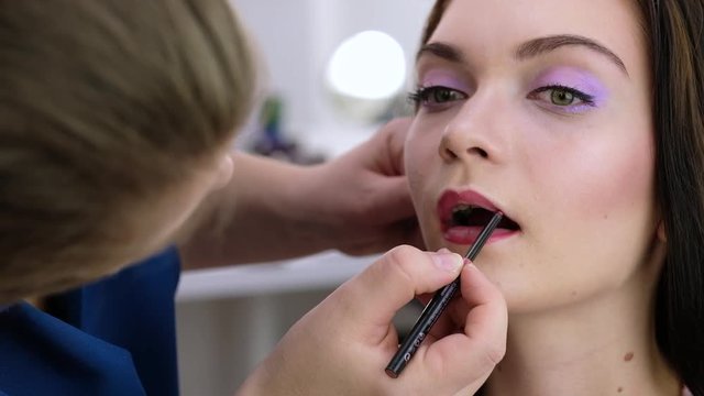 Make-up process, the face of a beautiful young woman and makeup artist's hand with a brush for lips