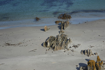 White sandy beach with outcrops of lichen covered rocks on Carcass Island in the Falkland Islands.