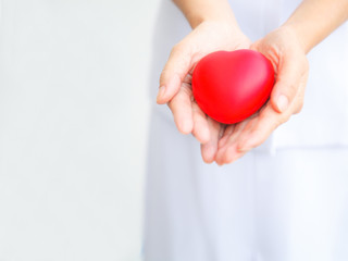 Red heart held by female nurse's hand, representing effort to deliver high quality service mind to patient. Professional, Specialist in white uniform isolated on white background.