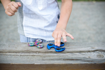 Boy holding blue and rainbow fidget spinners in his hands, view from above both gadgets spinning
