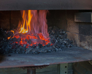 Fire blazes inside the dark coal forge heating up metal to become a set of spurs.
