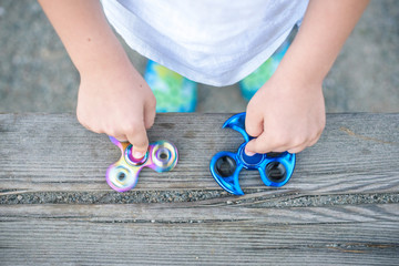 Boy holding blue and rainbow fidget spinners in his hands, view from above both gadgets spinning