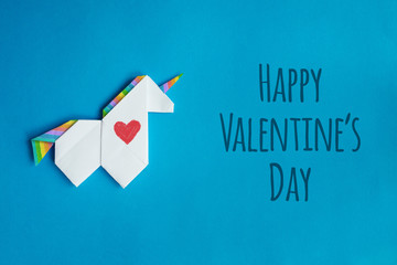 Handmade white trendy geometrical polygonal paper origami unicorn on blue background. Happy valentines day lettering, message, text. Holiday poster, postcard, banner.